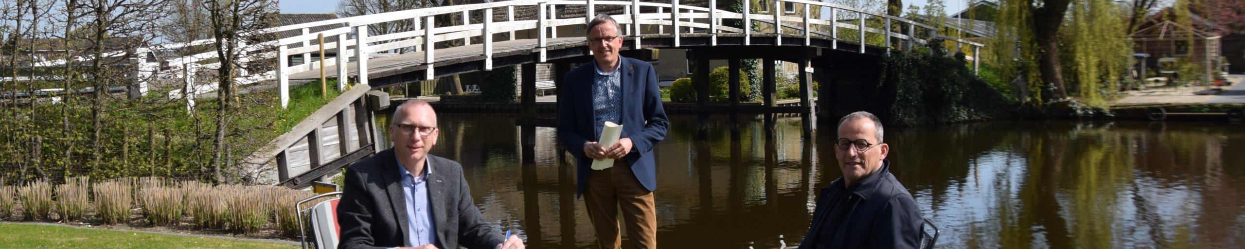 afbeelding van het tekenen van het contract door de betrokken partijen, met op de achtergrond de Pinkeveerse brug